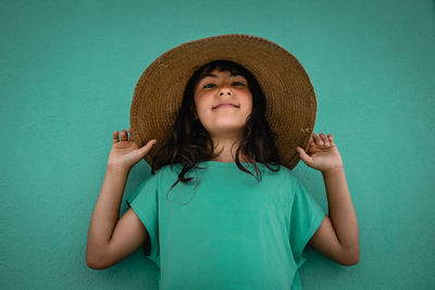 Portrait of girl in green t-shirt and straw hat against green wall