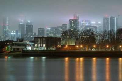 Illuminated city by river against sky at night