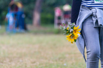 Low section of woman with yellow flower against blurred background