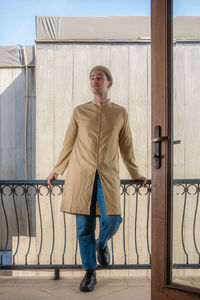Man who wears light brown kurta shirt and straight fit blue jeans standing at balcony.