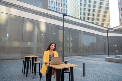 Full length of woman sitting on table in city