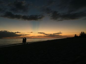 Silhouette people at beach against sky during sunset