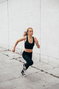 Portrait of young woman running by wall