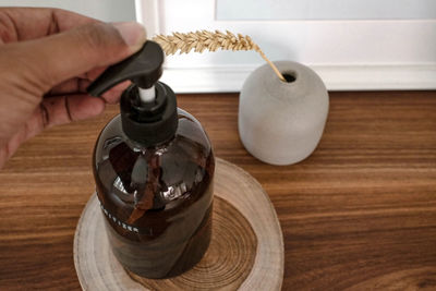 Hand sanitizer dispenser bottle with ceramic bottle on a wooden table in a room.
