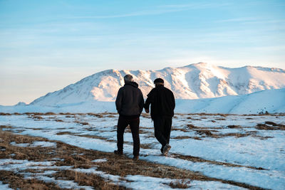 Rear view of man standing on snowcapped mountain against sky