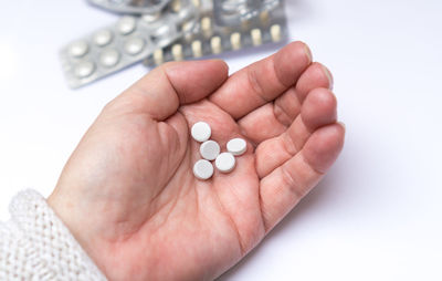 Close-up of hand holding pills on white table