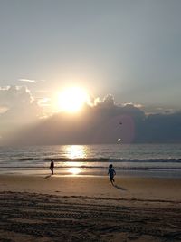 Silhouette people at beach against sky during sunset