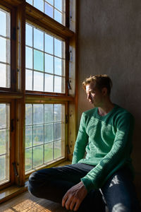 Man looking away while sitting on window at home