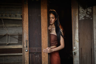 Portrait of young woman standing against wooden wall