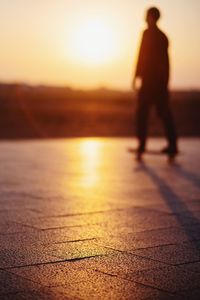 Silhouette man standing on footpath by street against sky during sunset