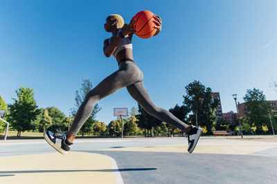 Young sportswoman with basketball jumping in sports court