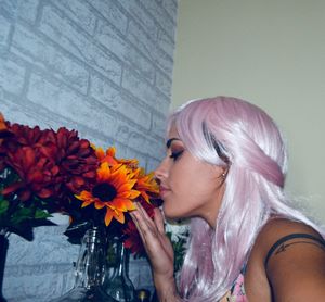 Close-up of woman with dyed pink hair smelling flowers at home