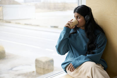 Woman drinking coffee sitting near window