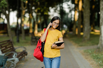 A pretty student girl with glasses and a red backpack is walking around the campus and talking 