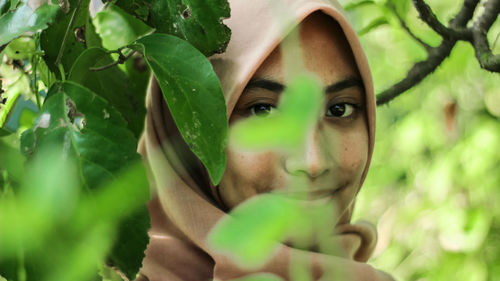 Close-up portrait of young woman with green leaves