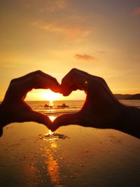 Silhouette hands making heart shape at beach against sky during sunset