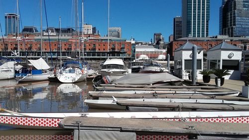 Sailboats moored on harbor by buildings against sky in city