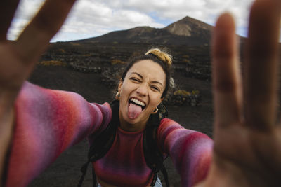 Happy woman sticking out tongue and taking selfie with landscape in background