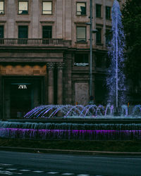 Illuminated fountain by building in city