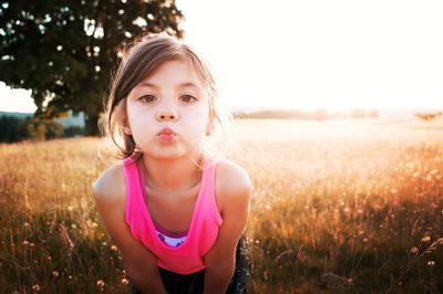 Portrait of girl puckering lips while standing on field during sunny day