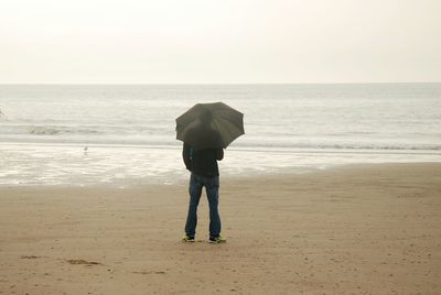 Man with umbrella standing at beach against clear sky