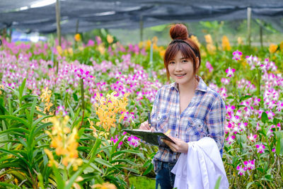 Portrait of smiling young woman standing by flowering plants