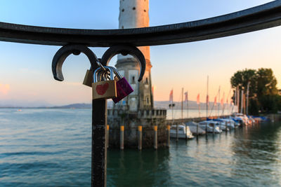 Padlocks hanging on railing by river against sky