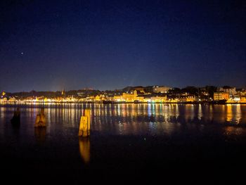 Illuminated buildings by lake against sky in city at night