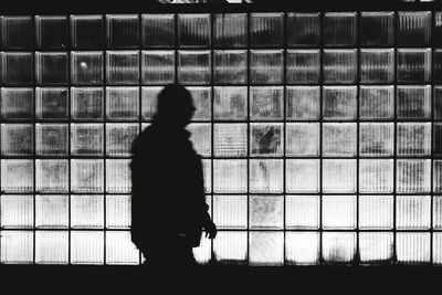 Silhouette man walking by glass wall