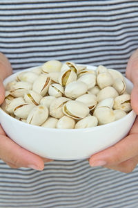 Midsection of person holding pistachio nuts in bowl