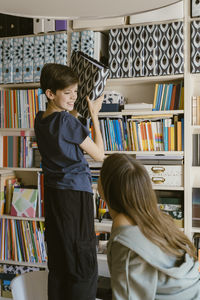 Smiling boy looking at sister while removing file from rack at home