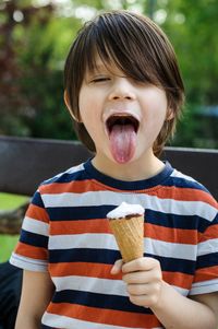 Boy sticking out tongue while eating ice cream at park