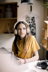 Girl wearing headphones sitting at desk while looking away