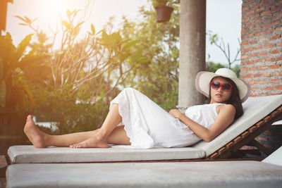 Full length portrait of young woman relaxing on lounge chair at yard