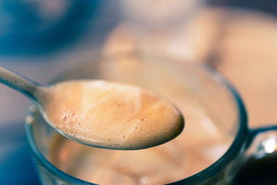 Close up cappuccino coffee in the spoon with glass.