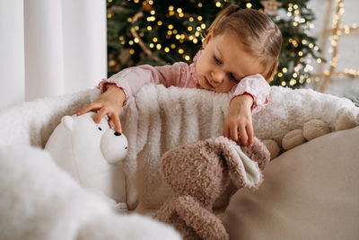 Cute toddler child waiting for presents at home after decorating christmas tree in eco style 