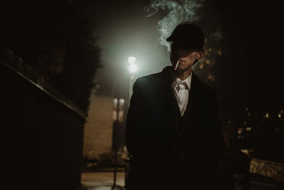 Man standing by illuminated light at night