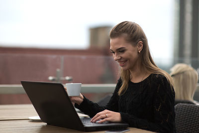 Smiling young woman using laptop while sitting at sidewalk cafe