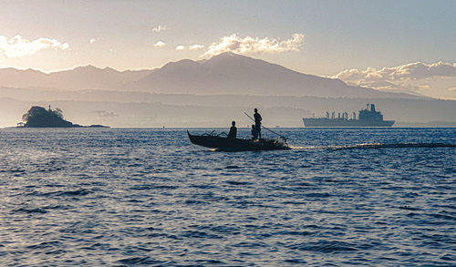 People sailing on sea against sky during sunset