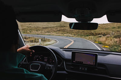 Unrecognizable man driving a car on an empty countryside road, view from the inside of the car