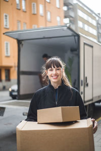 Portrait of smiling female mover carrying cardboard boxes