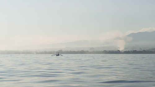 View of a far boat sailing in a light haze, returning to the beach