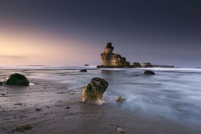 Rock formation on beach against sky during sunset
