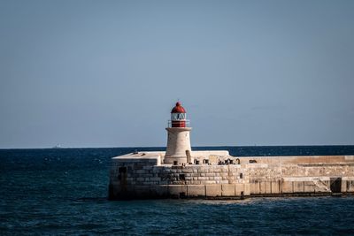 Lighthouse by sea against building against clear sky