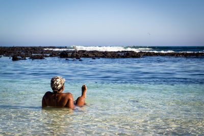 Rear view of shirtless man on sea against clear sky