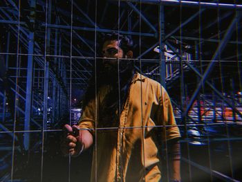 Portrait of young man standing against fence