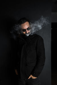 Young man smoking against black background