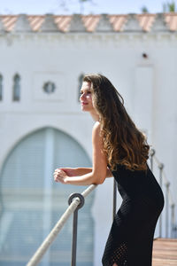 Side view of woman standing by railing against built structure