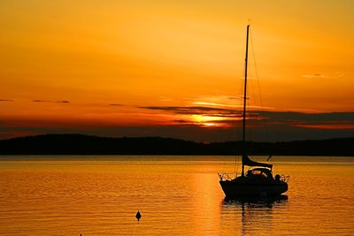 Silhouette sailboat in sea against orange sky