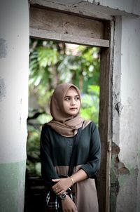 Young woman in hijab looking away while standing by abandoned building